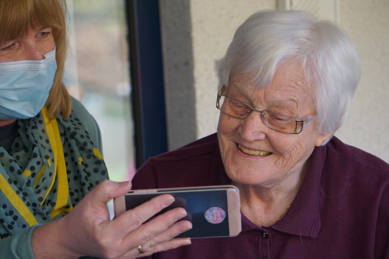 A caregiver showing a phone to a smiling older woman
