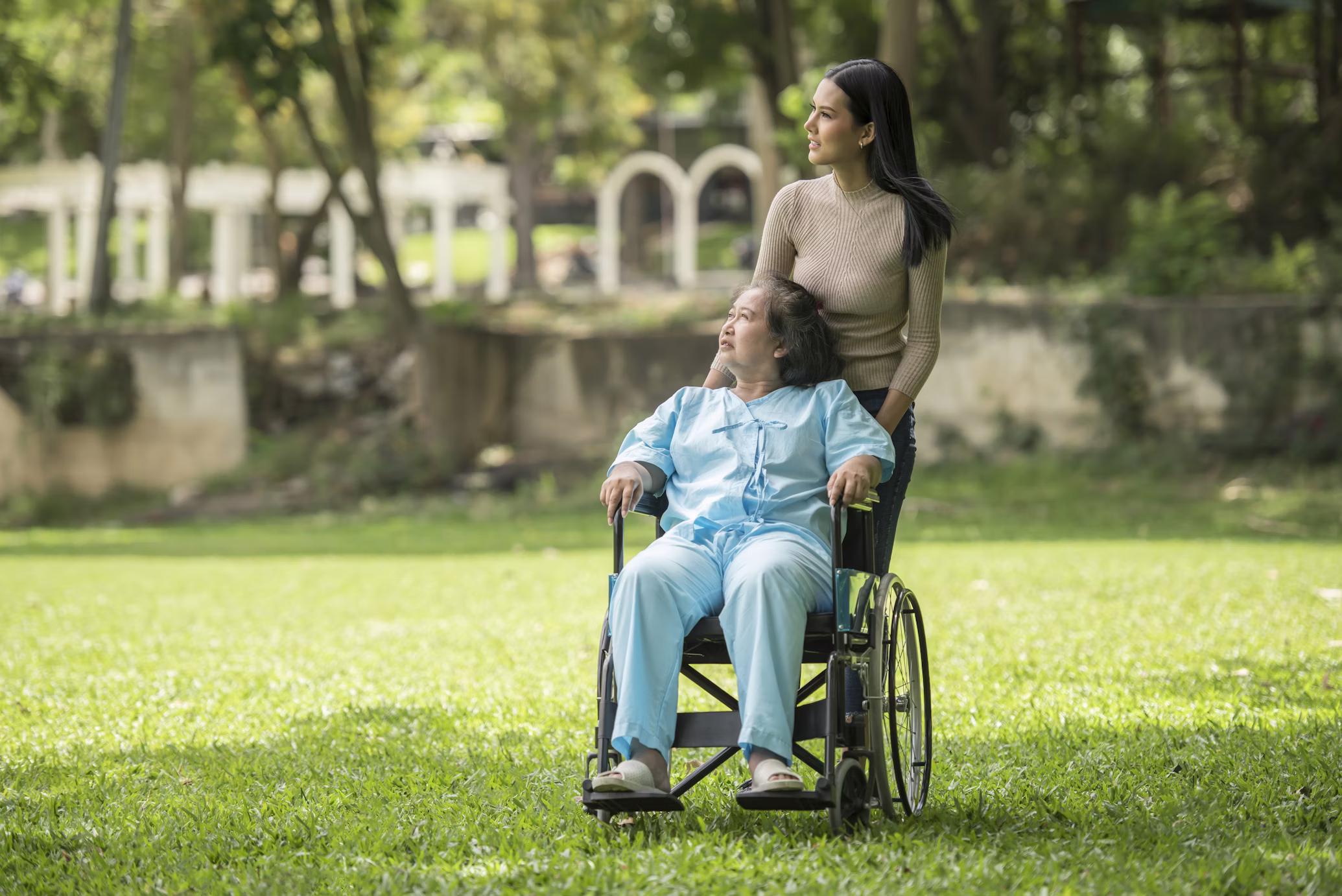 Caregiver pushing an elderly patient in a wheelchair through a park