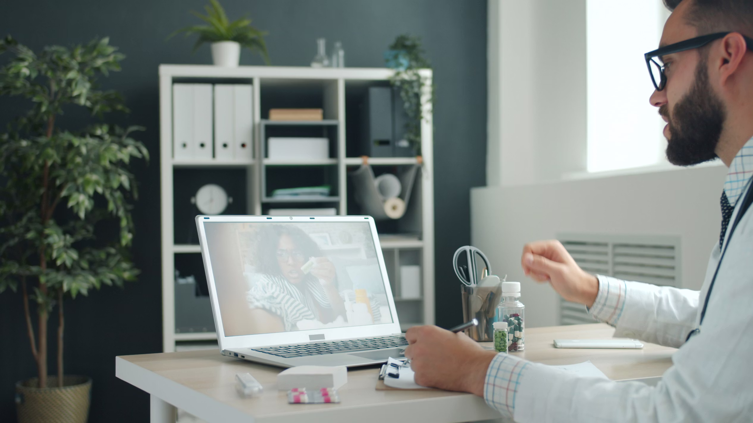 Physician on a video call with a patient, reviewing medications from his office