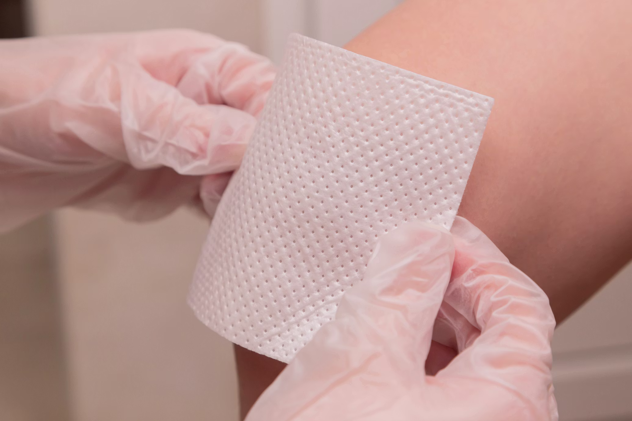 Gloved hands applying a sterile wound dressing to a patient's leg